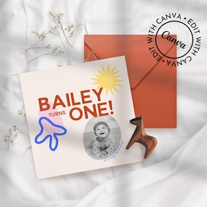 May include: A birthday card with the text "BAILEY TURNS ONE!" and a photo of a baby. The card has a sun graphic and a blue and pink abstract shape. An orange envelope and a wooden horse figurine are also present.