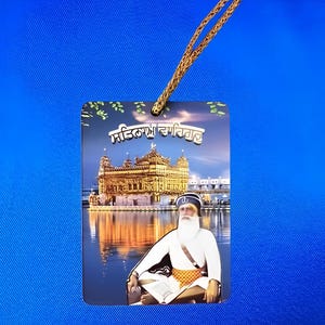 May include: Rectangular pendant featuring an image of a golden temple reflected in water, with a figure in white and a gold chain. The pendant has text at the top. The background is a solid blue.
