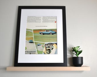 May include: Framed vintage advertisement for a 1967 Plymouth Barracuda. The ad features a light blue car on a winding road, with the text "You'll never want to go straight again." The frame is black.