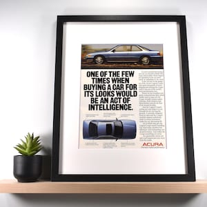 May include: Framed print featuring an Acura car advertisement. The ad includes a photo of a blue car and the text: "ONE OF THE FEW TIMES WHEN BUYING A CAR FOR ITS LOOKS WOULD BE AN ACT OF INTELLIGENCE." The frame is black.