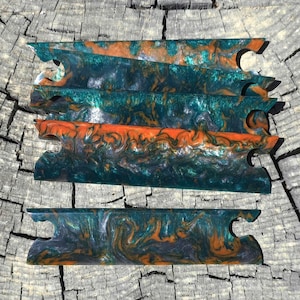 May include: A set of five rectangular resin blanks featuring a marbled pattern of deep teal, metallic copper, and black swirls. Each piece has a notched cutout on both ends, creating a uniform shape designed for crafting handles or knife scales.