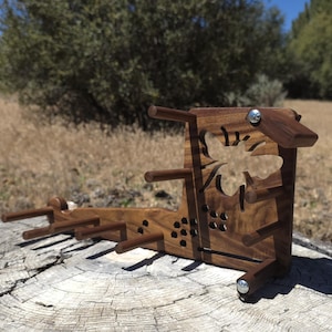 Puede incluir: Un soporte de madera de color marrón oscuro para ovillos o bobinas, con una silueta recortada de una abeja y varios pequeños recortes hexagonales en forma de panal, que cuenta con múltiples clavijas de madera horizontales.