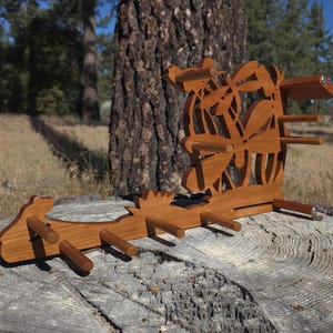 May include: A brown wooden wall-mounted rack featuring a cutout design of a dragonfly among leaves. The rack has a horizontal base with several protruding pegs for hanging items and a vertical back panel with a decorative nature-inspired motif.
