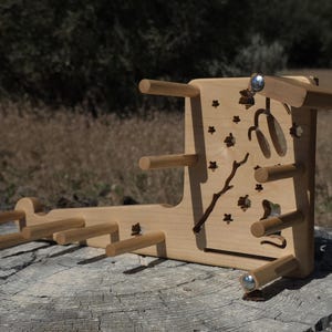 May include: A light-colored wooden yarn storage rack featuring a vertical panel with laser-cut star and branch motifs. The rack includes multiple horizontal pegs extending from the base and the vertical panel to hold yarn skeins or spools.
