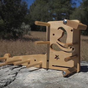 May include: A light-colored wooden yarn swift with a witch hat and star cutouts. The swift has multiple pegs for holding yarn and is designed to wind yarn into a ball. The swift is sitting on a tree stump.