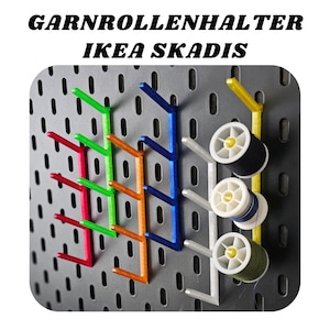 Op de afbeelding: Een close-up van een prikbord met vijf verschillende gekleurde garen houders, elk met een spoel garen. Het prikbord is gelabeld "GARNROLLENHALTER IKEA SKADIS".