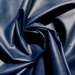 May include: Close-up of a swatch of navy blue leather fabric. The material is folded and draped, creating shadows and highlights that emphasize its texture and sheen. The fabric appears smooth and supple.