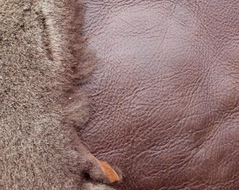 Może przedstawiać: Zbliżenie dwóch faktur: miękkiego, szaro-brązowego futra i ciemnobrązowej, teksturowanej skóry. Skóra ma pomarszczony wygląd, podczas gdy futro jest gęste i puszyste, tworząc kontrast.