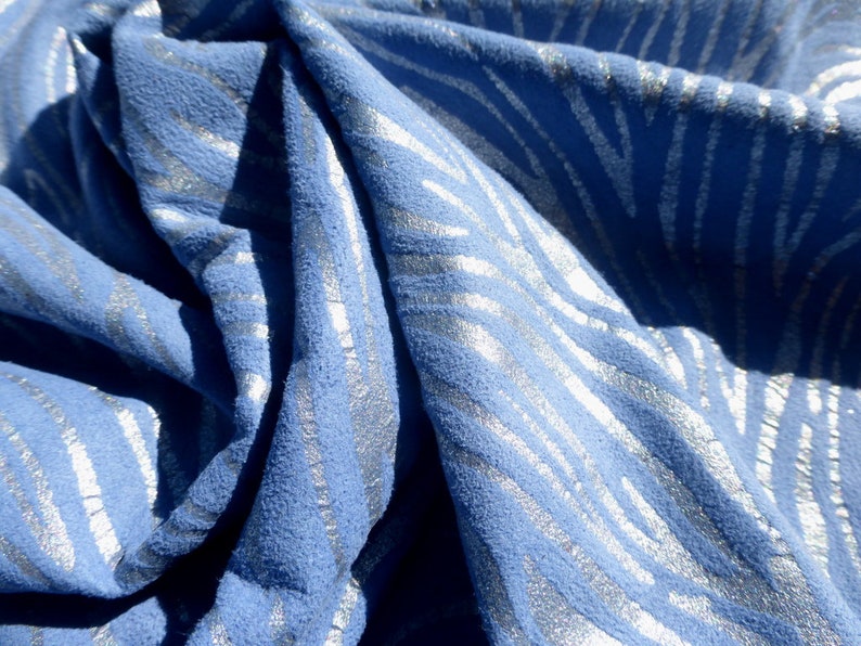 Op de afbeelding: Blauwe stof met een zilveren metallic patroon. De stof heeft een textuur en is gevouwen om het patroon te laten zien.