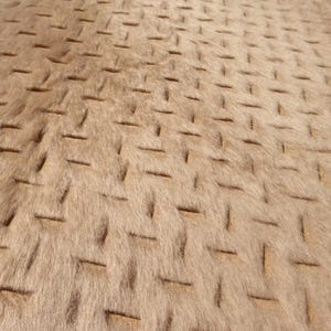 May include: Close-up of a textured, tan-colored fabric with a repeating pattern of rectangular indentations. The fabric has a soft, fur-like appearance, with a subtle sheen. The design creates a visual texture, suitable for upholstery or decorative purposes.