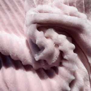 May include: A soft, plush pink blanket with a fluffy texture. The blanket is folded and arranged in a decorative way, creating a soft and inviting look.