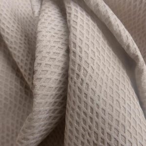 May include: Close-up of a soft, white fabric with a textured diamond pattern. The fabric is folded and draped, showing the texture and the way it drapes.