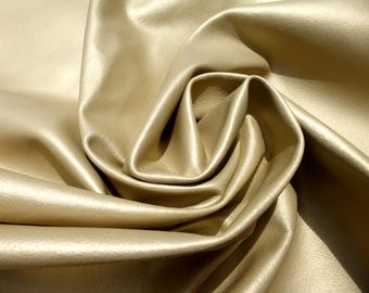 Pode incluir: Close-up de um tecido de couro dourado com dobras macias e um brilho sutil. O material parece liso e flexível, com uma leve textura visível na luz. Ideal para estofados ou projetos de moda.