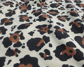 May include: A close-up of a white fabric with a brown and black leopard print pattern.