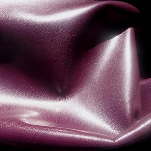 May include: Close-up of a deep purple leather fabric with a smooth, shiny surface. The fabric is folded and draped, creating soft folds and curves.