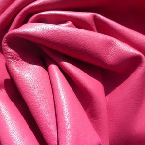 Può includere: Primo piano di un tessuto in pelle rosa vibrante, che mostra la sua trama e le pieghe. La pelle ha una finitura liscia e leggermente lucida.