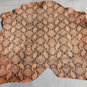 May include: A piece of brown leather with a snakeskin pattern. The leather has a light brown background with a darker brown snakeskin pattern.