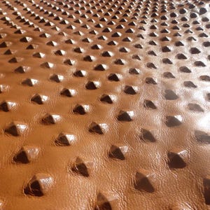 May include: Close-up of brown leather with a textured, raised pattern of small, diamond-shaped bumps.