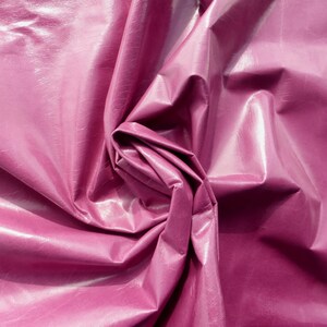 May include: Close-up of a deep pink, shiny fabric with a wrinkled, crinkled texture. The fabric is folded and twisted, creating a swirling pattern.