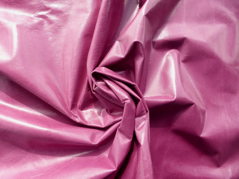 May include: Close-up of a deep pink, shiny fabric with a wrinkled, crinkled texture. The fabric is folded and twisted, creating a swirling pattern.