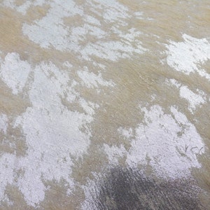 May include: A close-up of a textured surface with a silver metallic finish. The surface has a mottled appearance with areas of light and dark silver.
