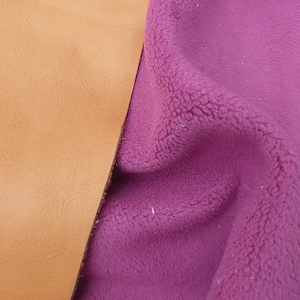 May include: A close-up of two fabric swatches. One is a light brown leather and the other is a deep pink fleece.