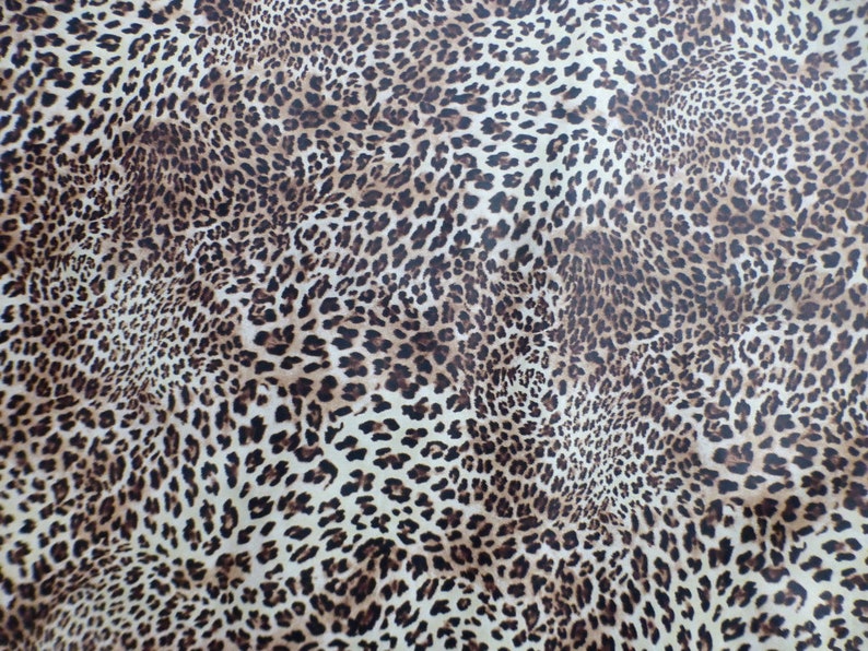 May include: A brown and white leopard print fabric with a subtle sheen. The fabric has a repeating pattern of brown spots on a white background.