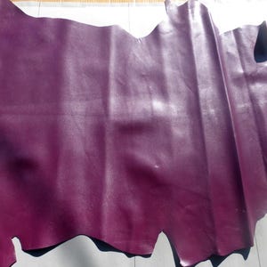 May include: A piece of purple leather with a smooth, shiny finish. The leather is folded and has a slightly irregular shape.