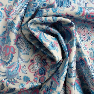 May include: A close-up of a fabric with a white background and a blue and pink floral pattern. The fabric is folded and the pattern is visible on both sides.