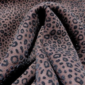 Puede incluir: Primer plano de una tela marrón con un estampado de leopardo negro. La tela está doblada, mostrando su textura y diseño. Las manchas de leopardo varían en tamaño, creando un efecto visual dinámico.