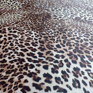 May include: A close-up of a brown and white leopard print fabric. The fabric has a soft, fuzzy texture.