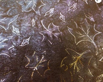 May include: Close-up of a dark brown surface with a metallic sheen, adorned with a pattern of stylized leaves. The leaves are outlined in white and gold, creating a contrasting design.