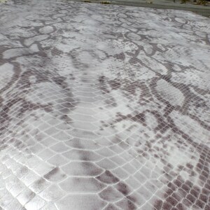 Op de afbeelding: Een close-up van een wit en grijs slangenhuidpatroon. Het patroon is geëmbost en heeft een subtiele glans.