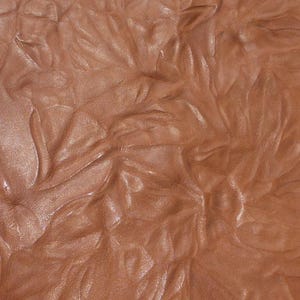 May include: Close-up of a brown leather surface with a textured, wrinkled pattern. The leather has a subtle sheen and appears soft and supple.