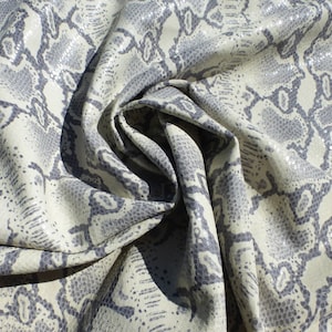 May include: A close-up of a white fabric with a gray snakeskin pattern. The fabric is folded and textured.