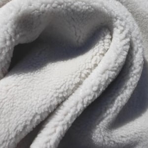 May include: Close-up of a soft, white, plush fabric with a textured, fuzzy surface. The material is folded, creating shadows and highlighting the depth of the texture. The fabric appears warm and inviting.