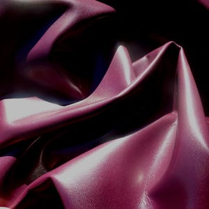 May include: Close-up of a deep burgundy fabric with a smooth, slightly shiny texture. The fabric is folded and draped, creating soft, flowing lines.