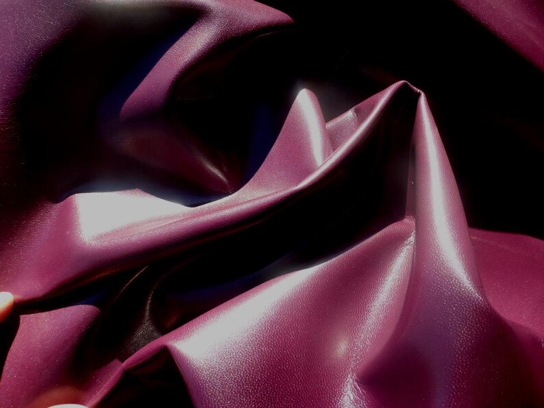 May include: Close-up of a deep burgundy fabric with a smooth, slightly shiny texture. The fabric is folded and draped, creating soft, flowing lines.