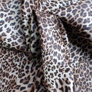 May include: Close-up of a brown and white leopard print fabric. The fabric is folded and has a soft, silky texture.