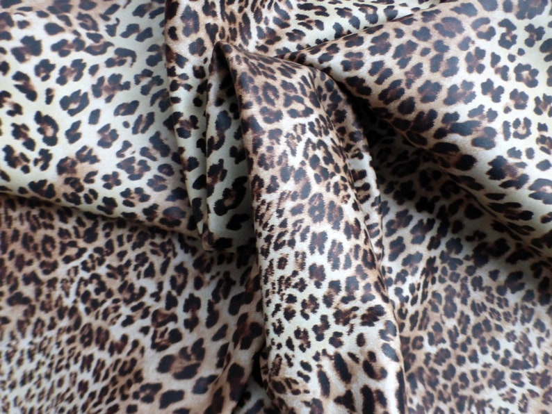 May include: Close-up of a brown and white leopard print fabric. The fabric is folded and has a soft, silky texture.