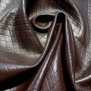 May include: Close-up of a brown quilted fabric with a diamond pattern. The fabric has a shiny, almost metallic finish.