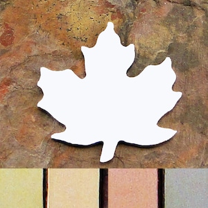 May include: A white metal maple leaf charm pendant. The charm is shown on a brown textured background. The charm is available in four different metal finishes: gold, silver, copper, and antique silver.