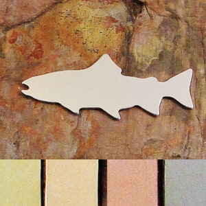 May include: A silver metal cutout of a fish, with a simple design. The fish is shown against a brown, textured background. The image also shows four color swatches: gold, silver, copper, and gray.