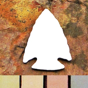 May include: A white arrowhead-shaped object against a textured, brown and orange background. The arrowhead has a triangular point and a notched base. The background has a mottled appearance with variations in color and texture.