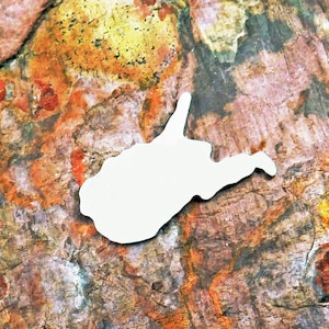 May include: A white metal cutout of the state of West Virginia. The cutout is on a background of brown, orange, and yellow textured rock.