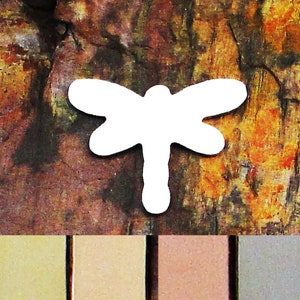 May include: White wooden dragonfly cutout against a brown, orange, and yellow abstract background. The dragonfly is a simple silhouette with no details.