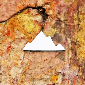 May include: White mountain silhouette pin on a textured brown and orange background.