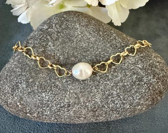 May include: A gold heart-shaped chain bracelet with a single white pearl charm.