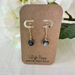 May include: A pair of gold earrings with iridescent abalone shell accents. The earrings are displayed on a brown card with the text "La Ruffa Designs Handmade. Unique Jewelry".
