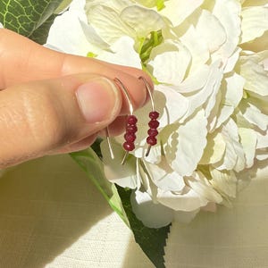 May include: A pair of silver hoop earrings with a row of small, red gemstone beads.